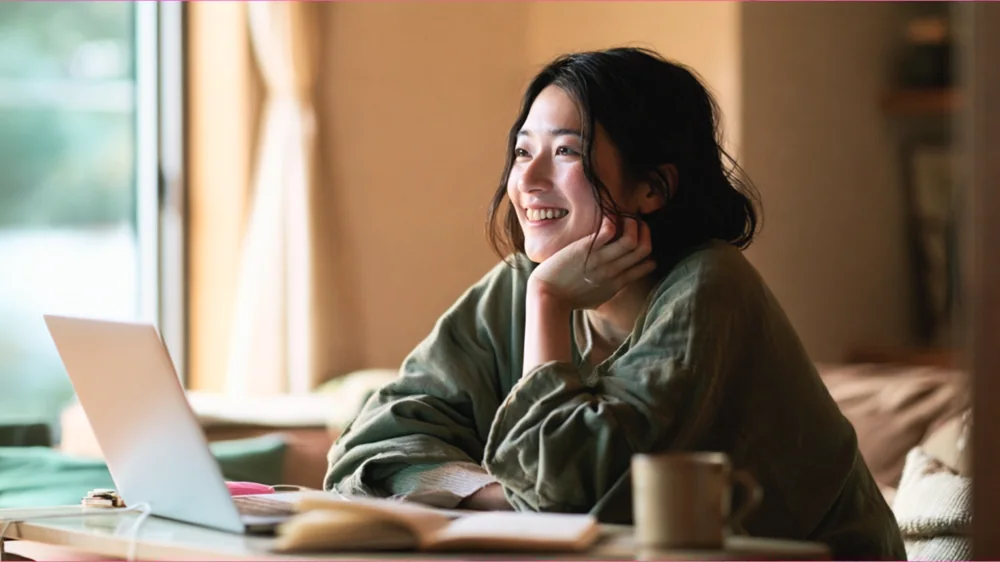 自宅のソファでノートパソコンに向かってほほえむ女性